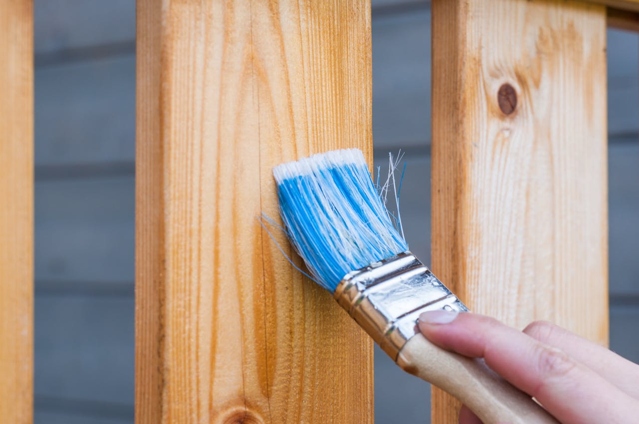 Mastering the First Impression: Your intriguing post title goes here A hand painting a wooden fence plank with a blue paintbrush outdoors. Perfect for DIY and renovation themes.