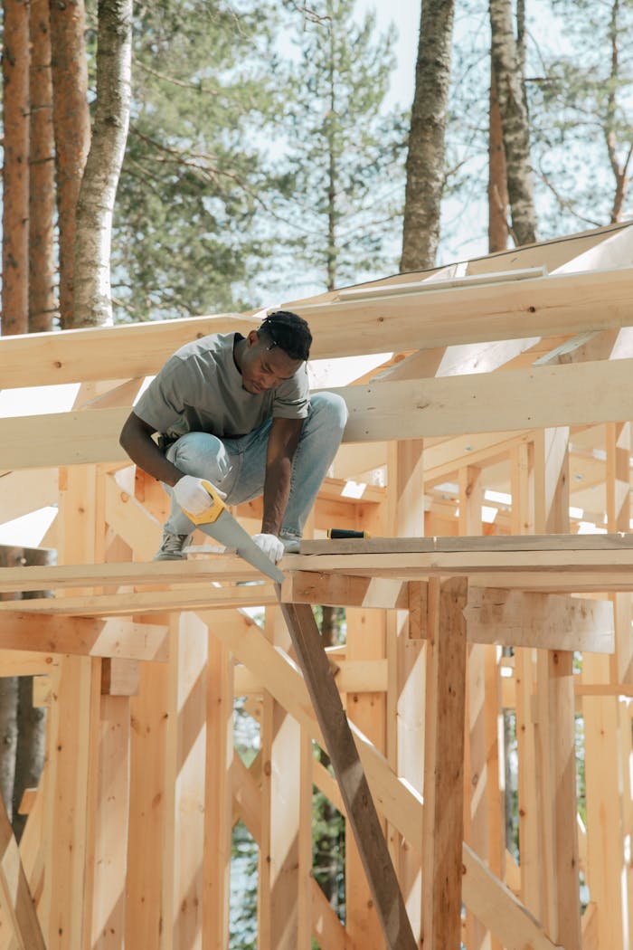 Man working with hand saw and gloves on wooden construction outdoors.